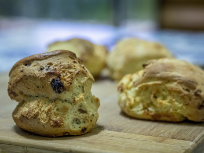 Freshly baked scones made with Basic Ingredients Scone Mix, displayed on a rustic wooden table, showcasing various flavors like cheese, blueberry, and pumpkin. Each scone looks golden and fluffy, perfect for a delightful snack or part of an elegant tea time spread